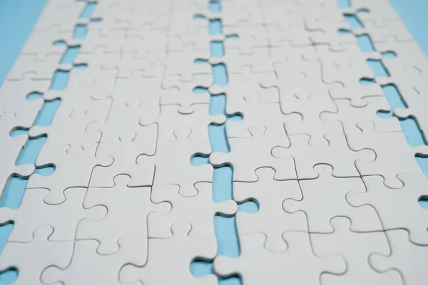 Missing jigsaw puzzle pieces. Business concept. Fragment of a folded white jigsaw puzzle and a pile of uncombed puzzle elements against the background of a blue surface.