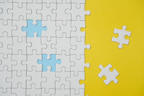 Missing jigsaw puzzle pieces. Business concept. Fragment of a folded white jigsaw puzzle and a pile of uncombed puzzle elements against the background of a yellow surface.