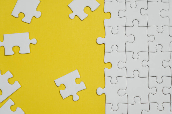 Missing jigsaw puzzle pieces. Business concept. Fragment of a folded white jigsaw puzzle and a pile of uncombed puzzle elements against the background of a yellow surface.