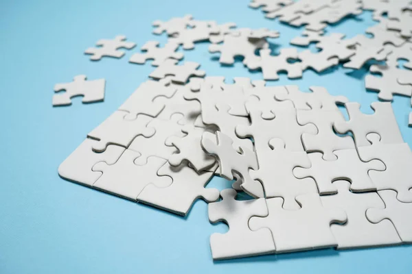 Missing jigsaw puzzle pieces. Business concept. Fragment of a folded white jigsaw puzzle and a pile of uncombed puzzle elements against the background of a blue surface.