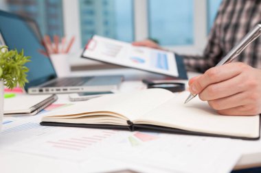 İş adamı bir masada otururken bir deftere yazar. Yeni modern bilgisayar ve iş stratejisiyle çalışan iş adamının silueti, seçici odaklanma