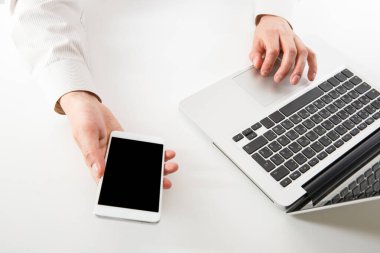 Dizüstü bilgisayar ve akıllı telefon üzerinde çalışan bir adam. Genç bir serbest çalışan. Akıllı telefon ve dizüstü bilgisayar kullanan adama yakın çekim