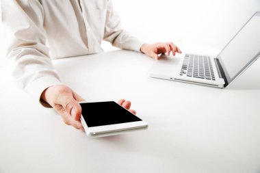 Dizüstü bilgisayar ve akıllı telefon üzerinde çalışan bir adam. Genç bir serbest çalışan. Akıllı telefon ve dizüstü bilgisayar kullanan adama yakın çekim