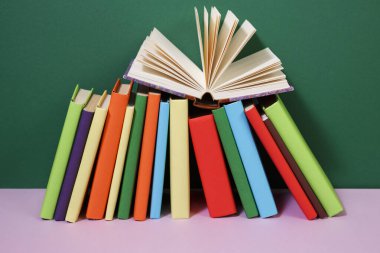 Kaliteli eski ciltli kitaplar, günlük, ahşap güverte masasında yelpaze sayfaları ve renkli arka planı olan kompozisyon. Kitaplar istifleniyor. Okula dönelim. Uzayı kopyala Eğitim geçmişi.