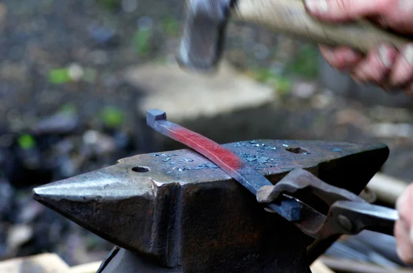 Ferreiro trabalhando metal com martelo na bigorna na forja Imagem De Stock