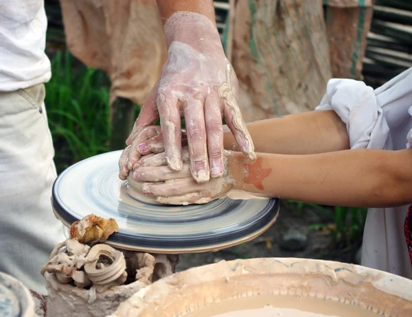 De handen van een pottenbakker helpen het kind maken een werper op een pottenbakkerij — Stockfoto