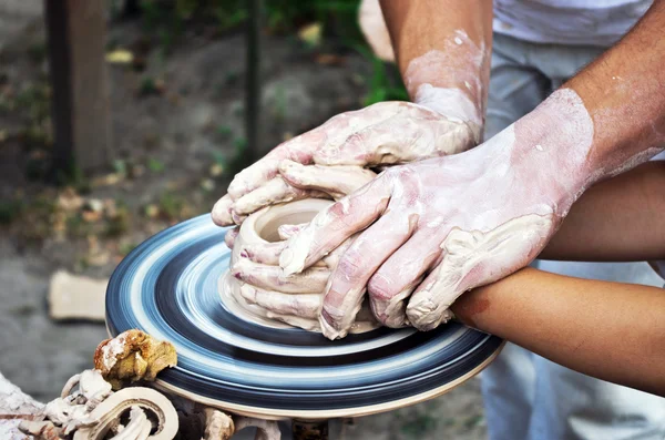 De handen van een pottenbakker helpen het kind maken een werper op een pottenbakkerij — Stockfoto