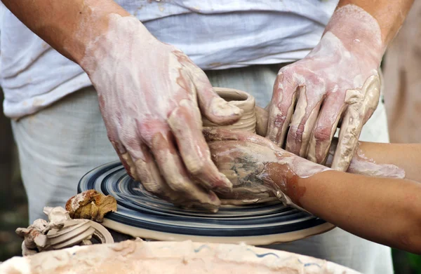 Les mains d'un potier aident l'enfant à faire un pichet sur une poterie — Photo