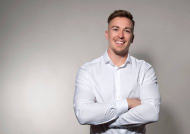 Gri arka planda beyaz gömlekli, gülümseyen yakışıklı bir genç.