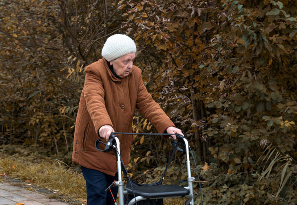 Пожилая женщина выходит на прогулку осенью с помощью ходунков, чтобы насладиться свежим воздухом