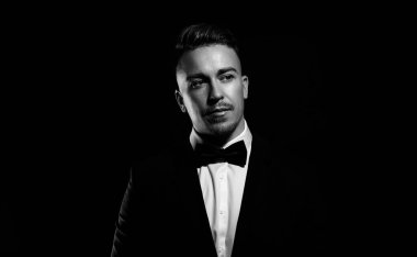 Siyah arka planda siyah beyaz poz veren takım elbiseli yakışıklı bir genç.