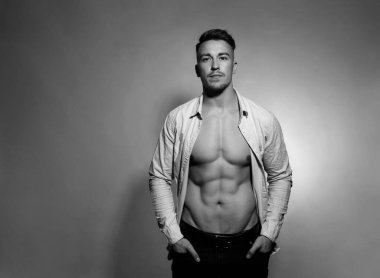 Formda ve atletik yapılı yakışıklı bir vücut geliştirici gri arka planda spor ceket giyiyor.