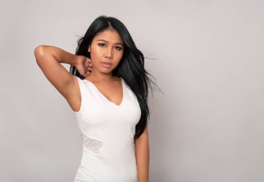 Gri arka planda uzun siyah saçlı güzel Asyalı kadın poz veriyor.