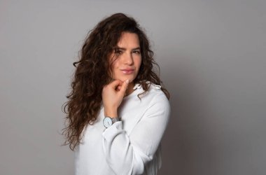 Gri arka planda uzun kıvırcık saçlı güzel bir kadın poz veriyor.