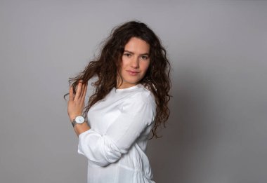 Gri arka planda uzun kıvırcık saçlı güzel bir kadın poz veriyor.