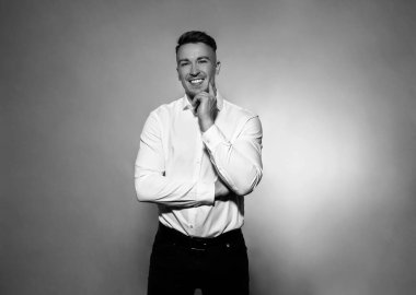 Gri arka planda beyaz gömlekli, gülümseyen yakışıklı bir genç.