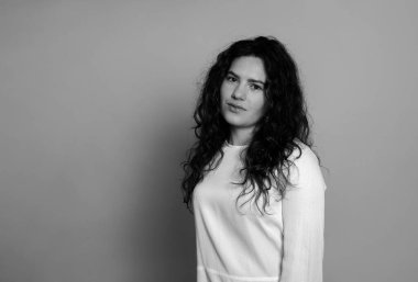 Gri arka planda uzun kıvırcık saçlı güzel bir kadın poz veriyor.