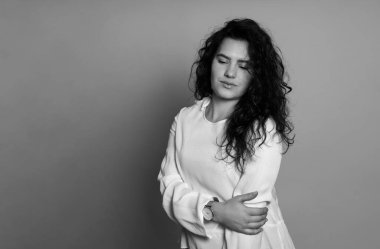 Gri arka planda uzun kıvırcık saçlı güzel bir kadın poz veriyor.