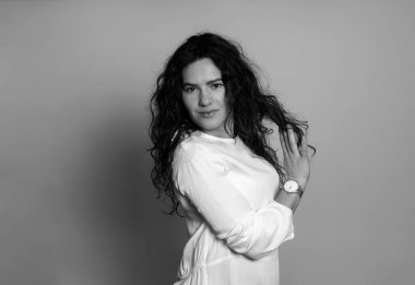 Gri arka planda uzun kıvırcık saçlı güzel bir kadın poz veriyor.