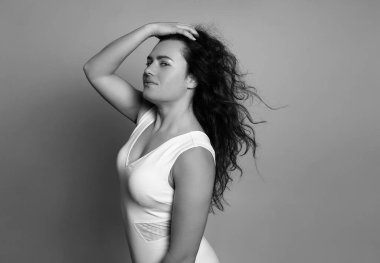 Gri arka planda uzun kıvırcık saçlı güzel bir kadın poz veriyor.