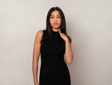 Gri arka planda uzun siyah saçlı güzel bir kadın poz veriyor.