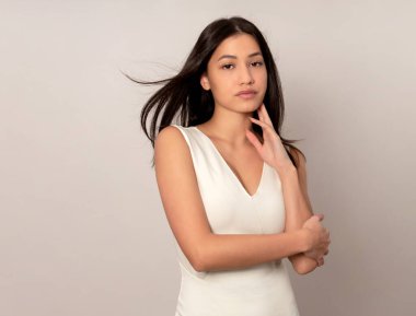 Gri arka planda uzun siyah saçlı güzel bir kadın poz veriyor.