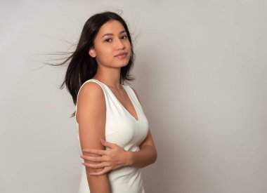 Gri arka planda uzun siyah saçlı güzel bir kadın poz veriyor.