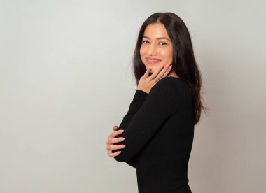 Gri arka planda uzun siyah saçlı güzel bir kadın poz veriyor.