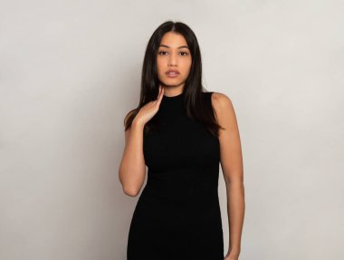 Gri arka planda uzun siyah saçlı güzel bir kadın poz veriyor.