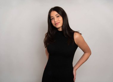 Gri arka planda uzun siyah saçlı güzel bir kadın poz veriyor.