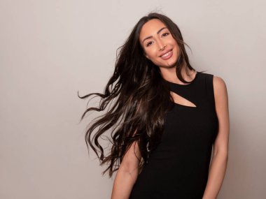 Gri arka planda uzun siyah saçlı ve doğal makyajlı güzel bir kadın. 