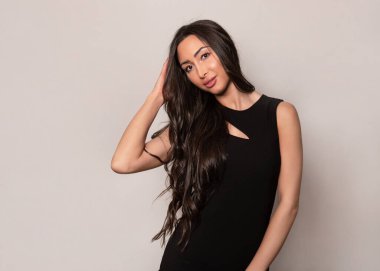 Gri arka planda uzun siyah saçlı ve doğal makyajlı güzel bir kadın. 