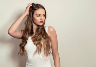 Gri arka planda uzun, parlak ve sağlıklı saçları olan güzel bir genç kadın.