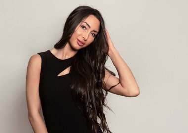 Gri arka planda uzun siyah saçlı ve doğal makyajlı güzel bir kadın. 