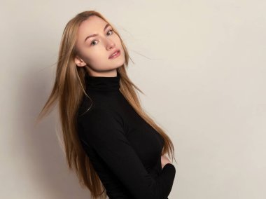 Sarışın, uzun, parlak ve sağlıklı saçları olan, gri arka planda poz veren güzel bir genç kadın.