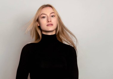 Sarışın, uzun, parlak ve sağlıklı saçları olan, gri arka planda poz veren güzel bir genç kadın.