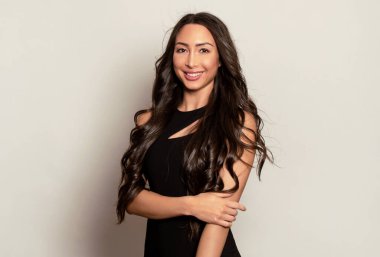 Gri arka planda uzun siyah saçlı ve doğal makyajlı güzel bir kadın. 