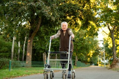 Yaşlı, mutlu, gri saçlı bir kadın. Parkta yürürken gülümserken Walker 'ın yardımıyla. 