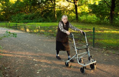 Yaşlı, mutlu, gri saçlı bir kadın. Parkta yürürken gülümserken Walker 'ın yardımıyla. 