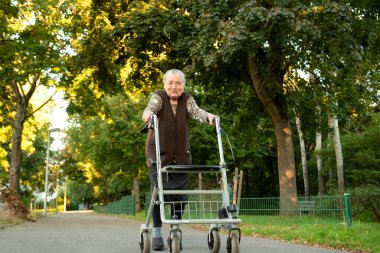 Yaşlı, mutlu, gri saçlı bir kadın. Parkta yürürken gülümserken Walker 'ın yardımıyla. 
