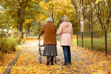 Kadın ve yaşlı annesi, sonbahar yapraklarıyla kaplı parkta yürüyüş yapıyor, aile zamanlarını birlikte geçiriyorlar.