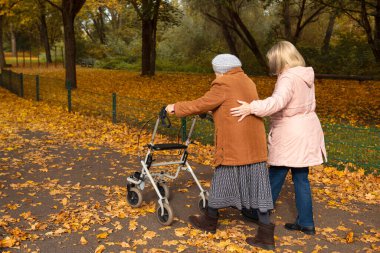 Kadın ve yaşlı annesi, sonbahar yapraklarıyla kaplı parkta yürüyüş yapıyor, aile zamanlarını birlikte geçiriyorlar.
