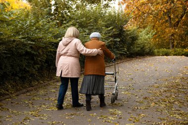 Kadın ve yaşlı annesi, sonbahar yapraklarıyla kaplı parkta yürüyüş yapıyor, aile zamanlarını birlikte geçiriyorlar.