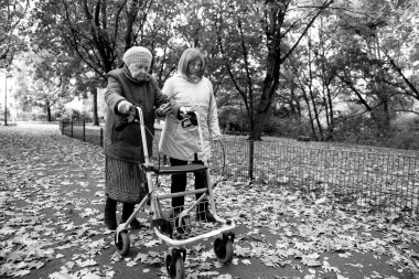 Kadın ve yaşlı annesi, sonbahar yapraklarıyla kaplı parkta yürüyüş yapıyor, aile zamanlarını birlikte geçiriyorlar.