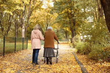 Kadın ve yaşlı annesi, sonbahar yapraklarıyla kaplı parkta yürüyüş yapıyor, aile zamanlarını birlikte geçiriyorlar.