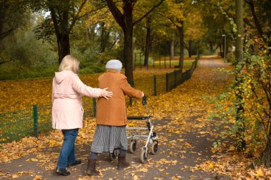 Kadın ve yaşlı annesi, sonbahar yapraklarıyla kaplı parkta yürüyüş yapıyor, aile zamanlarını birlikte geçiriyorlar.
