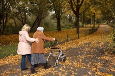 Kadın ve yaşlı annesi, sonbahar yapraklarıyla kaplı parkta yürüyüş yapıyor, aile zamanlarını birlikte geçiriyorlar.