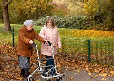 Kadın ve yaşlı annesi, sonbahar yapraklarıyla kaplı parkta yürüyüş yapıyor, aile zamanlarını birlikte geçiriyorlar.