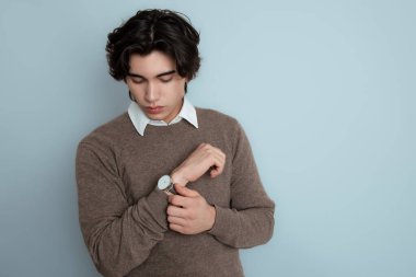 Metal kol saati takan, şık, rahat giyimli yakışıklı bir genç.