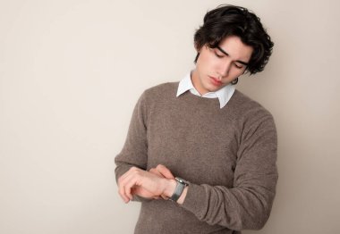 Metal kol saati takan, şık, rahat giyimli yakışıklı bir genç.